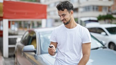 Young hispanic man smiling confident holding key of new car at street