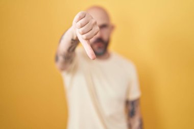 Sarı arka planda duran İspanyol dövmeli adam mutsuz ve kızgın görünüyor. Reddedilmiş ve olumsuz. kötü ifade. 