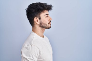 Hispanic man with beard standing over white background looking to side, relax profile pose with natural face and confident smile. 