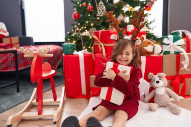 Sevimli İspanyol kız evde Noel ağacının yanında oturmuş hediyesini kucaklıyor.