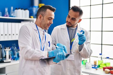 Two men scientists writing on document holding test tube at laboratory