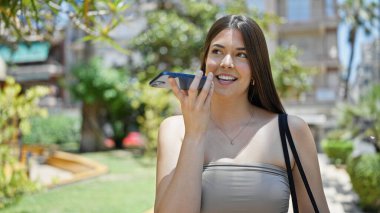Genç, güzel İspanyol kadın parkta akıllı telefonuyla sesli mesaj yolluyor.