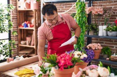 Young chinese man florist writing on notebook reading document at florist