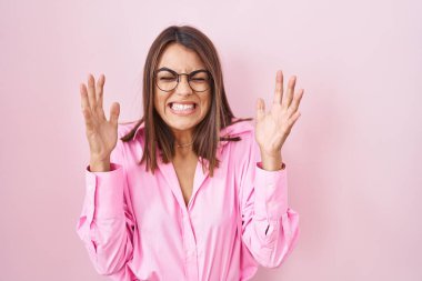Pembe arka planda duran gözlüklü genç İspanyol kadın başarı için çıldırıyor ve çıldırıyor kollarını kaldırıyor ve gözleri kapalı heyecanla bağırıyor. Kazanan konsept 