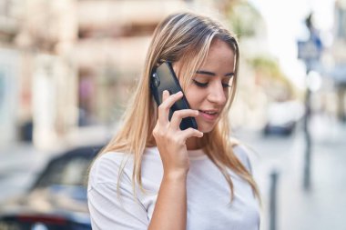 Genç sarışın kadın gülümsüyor. Kendine güveni tam. Akıllı telefondan konuşuyor.