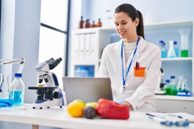 Laboratuvarda çalışan genç ve güzel İspanyol bilim kadını laptopu kullanıyor.