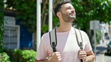 Sırt çantalı genç İspanyol turist parka gülümsüyor.