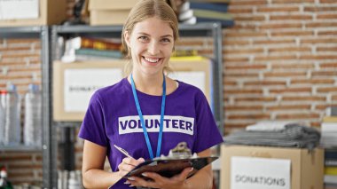 Young blonde woman volunteer smiling confident writing on checklist at charity center clipart