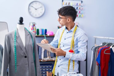 Young hispanic man tailor drawing on notebook at tailor shop