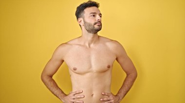 Genç İspanyol turist üstsüz duruyor ciddi bir yüz ifadesiyle yalıtılmış sarı arka plana bakıyor.