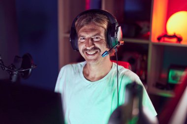 Kumarhanedeki masada kendinden emin gülümseyen sarışın genç adam.