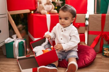 Sevimli İspanyol bebek Noel hediyesini açıyor. Evde yerde oturuyor.