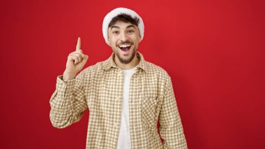 Genç Arap adam, izole edilmiş kırmızı arka plan üzerinde fikir ifadesi olan noel şapkası takıyor.