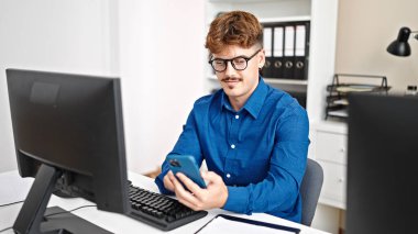 Genç İspanyol iş adamı ofiste gülümseyen akıllı telefon kullanıyor.