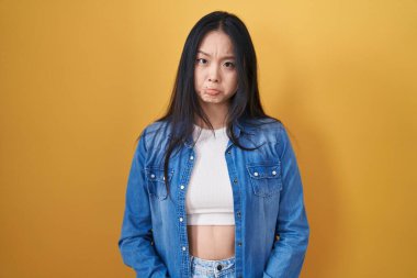 Sarı arka planda duran genç Asyalı kadın üzgün ve endişeli, sinirli ve korkmuş bir şekilde ağlıyor. hüzünlü ifade. 