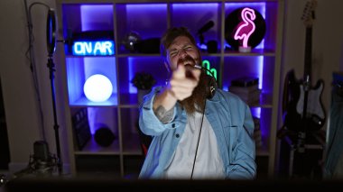 Neşeli genç kızıl saçlı flama destansı zaferini kutluyor. Adam video oyunu oynuyor, oyun odasındaki kamerayı işaret ediyor.