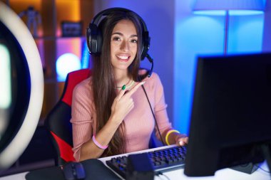 Yüzünde mutlu ve doğal bir ifadeyle elleri ve parmaklarıyla işaret eden bir gülümseme ile video oyunları oynayan genç İspanyol kadın. 