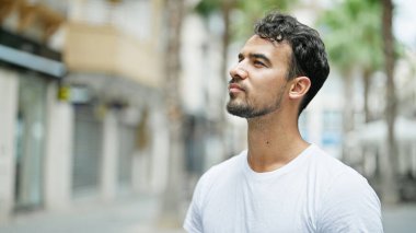 Latin kökenli genç adam ciddi bir ifadeyle sokağa bakıyor.