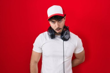 Sakallı, oyuncu şapkası takan ve kulaklık takan İspanyol bir adam. Şok suratlı, şüpheci ve alaycı görünüyor. 