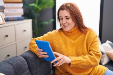 Young beautiful plus size woman using touchpad sitting on sofa at home