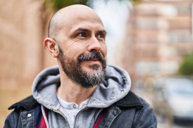 Genç kel adam gülümsüyor. Kendinden emin bir şekilde caddeye bakıyor.