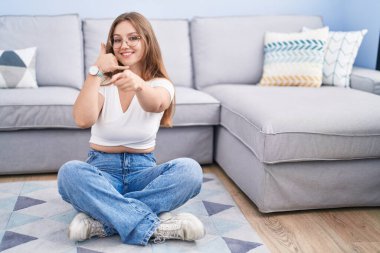 Oturma odasında yerde oturmuş gülümseyen beyaz bir kadın telefon jesti hakkında konuşuyor ve seni işaret ediyor. Ara beni.. 