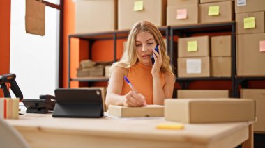 Genç sarışın kadın ecommerce iş işçisi. Ofiste paket üzerinde akıllı telefon yazısıyla konuşuyor.