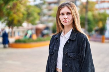 Young blonde woman standing with serious expression at park