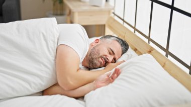 Gri saçlı adam yatakta uzanıyor, yatak odasında uyuyor.