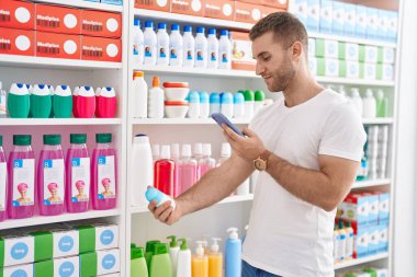 Genç beyaz adam müşterisi akıllı telefondan eczanedeki deodoranta fotoğraf çekiyor.