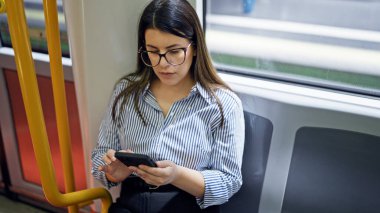 Genç ve güzel İspanyol kadın metroda oturmuş akıllı telefon kullanıyor.