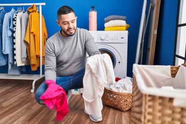 Young latin man smiling confident washing clothes at laundry room