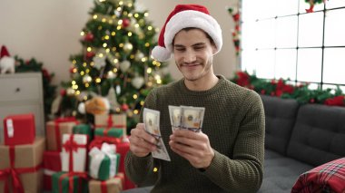 Genç İspanyol adam evdeki Noel ağacının yanındaki koltukta oturmuş dolar sayıyor.