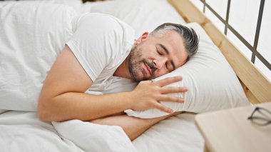 Gri saçlı adam yatakta uzanıyor, yatak odasında uyuyor.