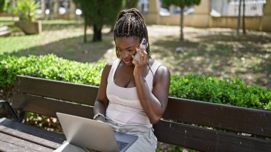 Akıllı telefondan konuşan Afro-Amerikalı bir kadın. Parkta bankta oturuyor.