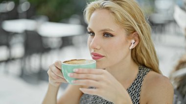 Genç sarışın kadın kahve içiyor kahve dükkanının terasında müzik dinliyor.