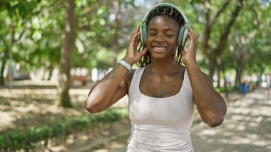 Parkta gülümseyen müzik dinleyen Afrikalı Amerikalı kadın.