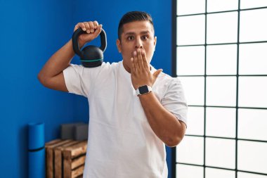 Ağzı elle kaplayan dambıllar kullanan İspanyol genç bir adam, şaşırdı ve hata yapmaktan korktu. şaşırmış ifade 