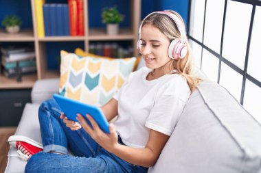 Sarışın genç kadın dokunmatik yastıkta video izliyor. Evdeki kanepede oturuyor.