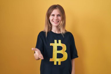 Sarışın, beyaz kadın bitcoin tişört giyiyor. Gülümsüyor. Avuç içi dolusu yardım eli uzatıyor ve kabulleniyor.. 