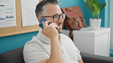 Gri saçlı iş adamı akıllı telefondan konuşuyor. Ofiste gülümsüyor.