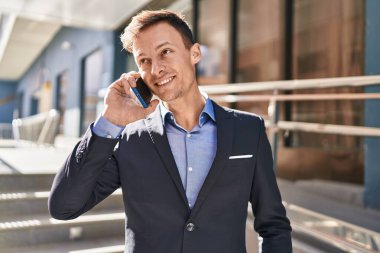 Genç iş adamı gülümseyerek caddede akıllı telefonla konuşuyor.