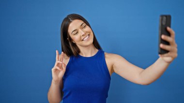 Genç, güzel, İspanyol bir kadın gülümsüyor. Kendine güveni tam. Akıllı telefonun yanında özçekim yapıyor.