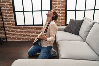 Genç beyaz adam evde yerde elektro gitar çalıyor.