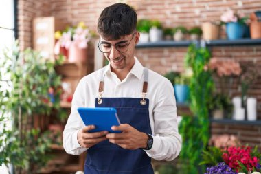 Young hispanic man florist smiling confident using touchpad at florist