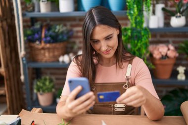 Çiçekçide akıllı telefon ve kredi kartı kullanan güzel İspanyol bir çiçekçi.