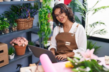 Young beautiful hispanic woman florist smiling confident using laptop at flower shop