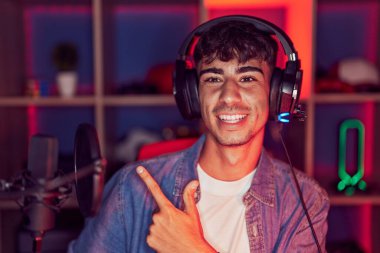 Genç İspanyol adam video oyunları oynuyor. Neşeli bir şekilde gülümsüyor. Elleri ve parmakları yana doğru. 