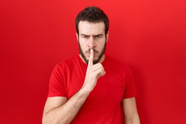Gündelik kırmızı tişört giyen genç İspanyol adam dudaklarında parmaklarıyla sessiz olmak istiyor. sessizlik ve gizli konsept. 