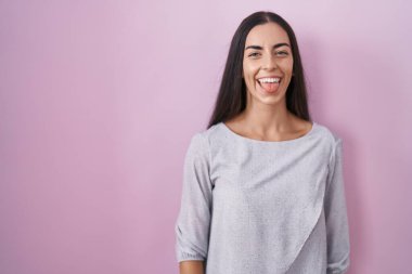 Pembe arka planda duran esmer kadın komik bir ifadeyle mutlu bir şekilde dilini dışarı çıkarıyor. duygu kavramı. 